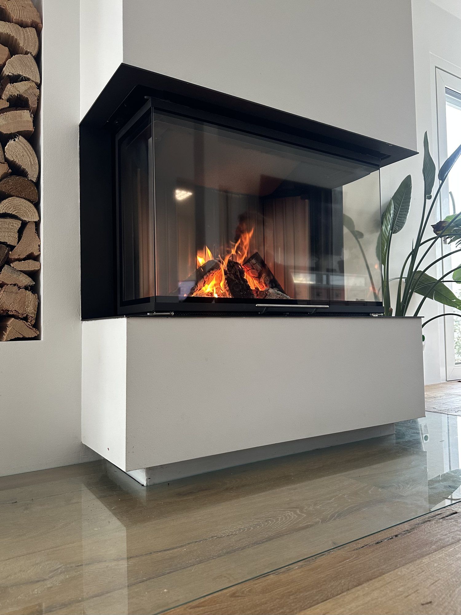 Detail eines Heizkamins mit großer Eck-Glasscheibe und lodernden Flammen
