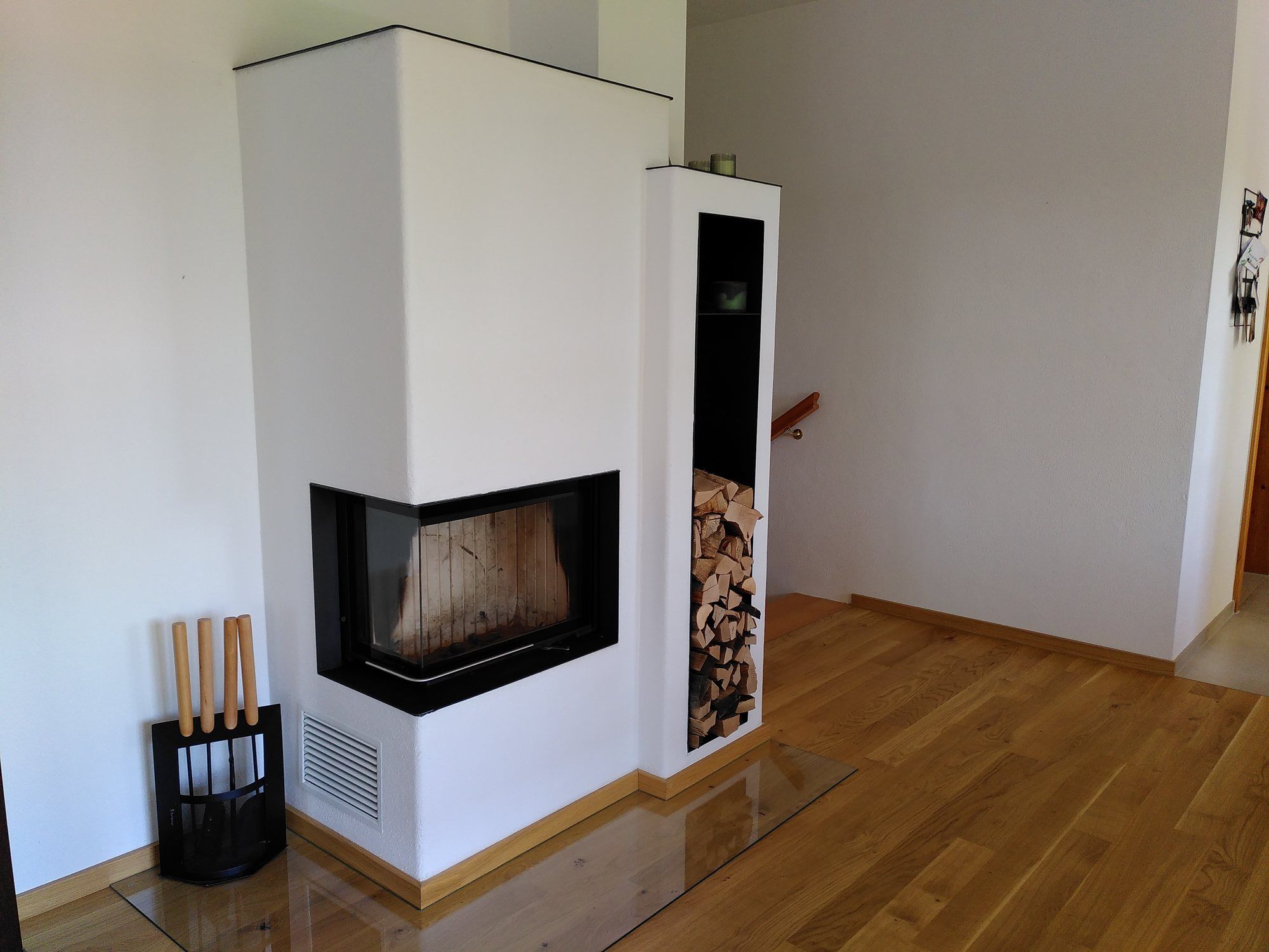 Weiß verputzter Eck-Heizkamin mit integriertem Holzfach auf einer Glasbodenplatte
