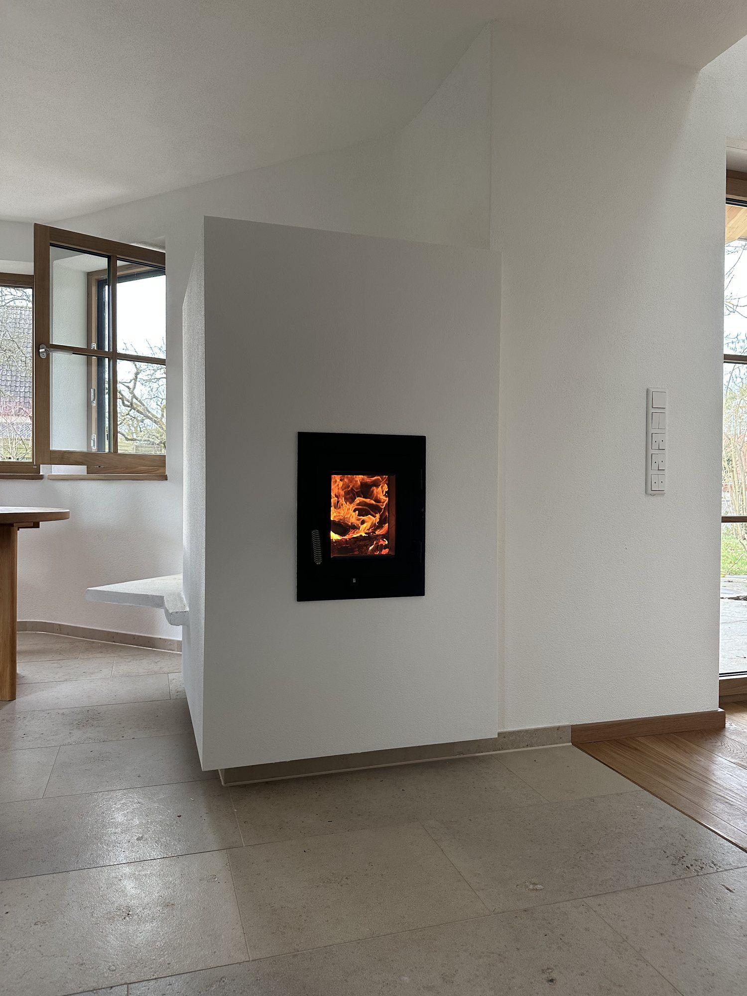 Weißer Kamin als frei stehender Raumteiler mit kleiner Sichtscheibe und brennendem Feuer